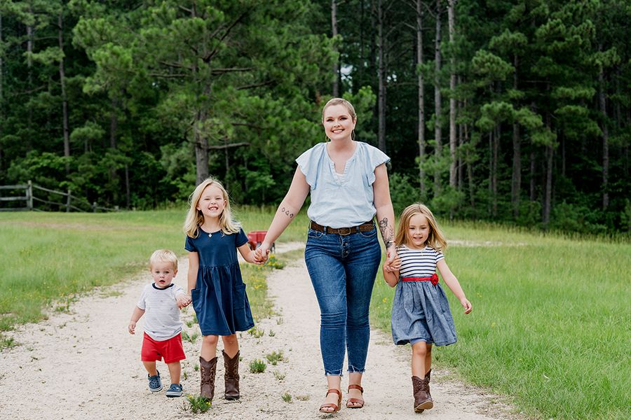 A woman smiling and walking with her children in nature.