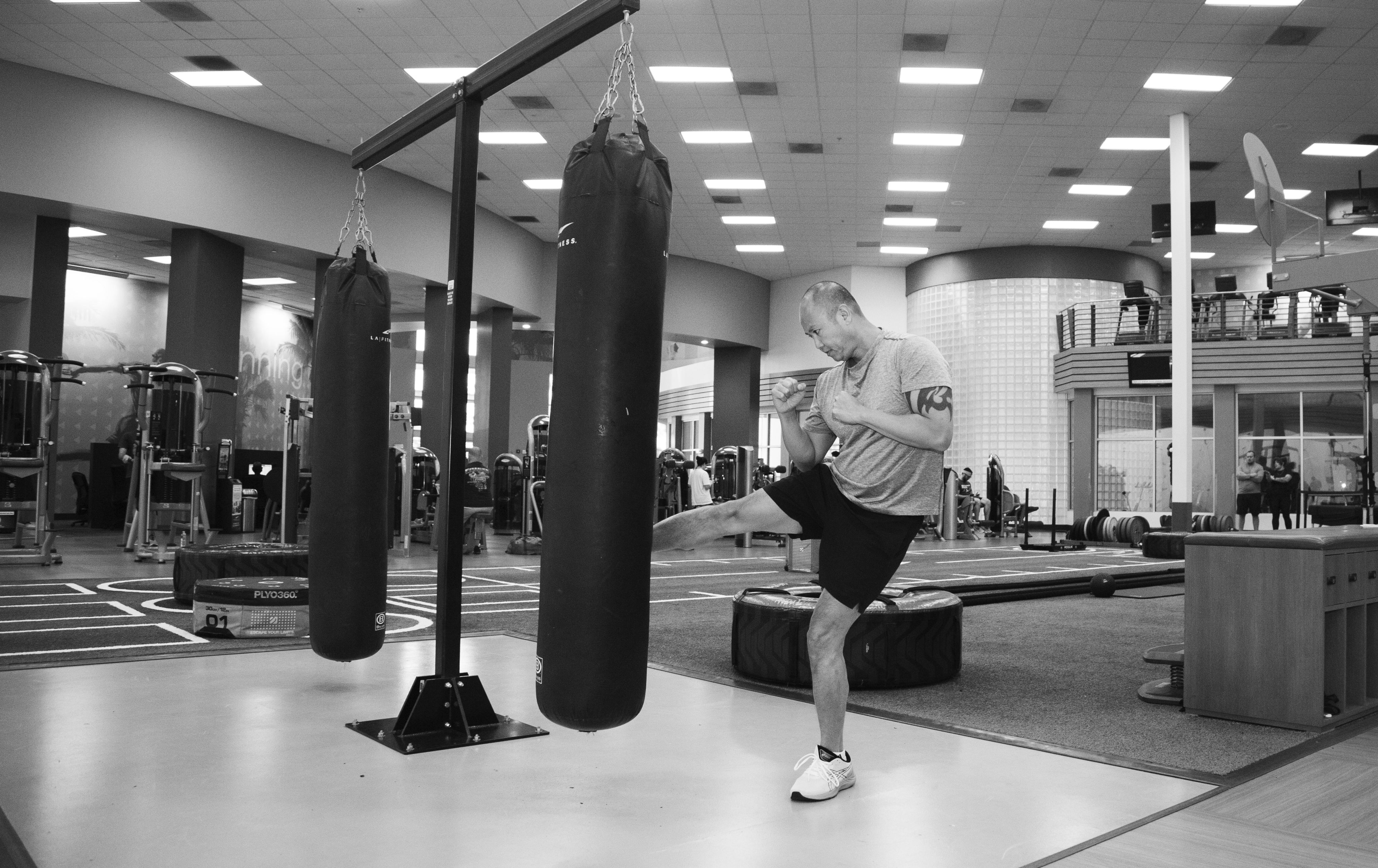 An image of a man with gout working out at the gym, kicking a kick-boxing bag.