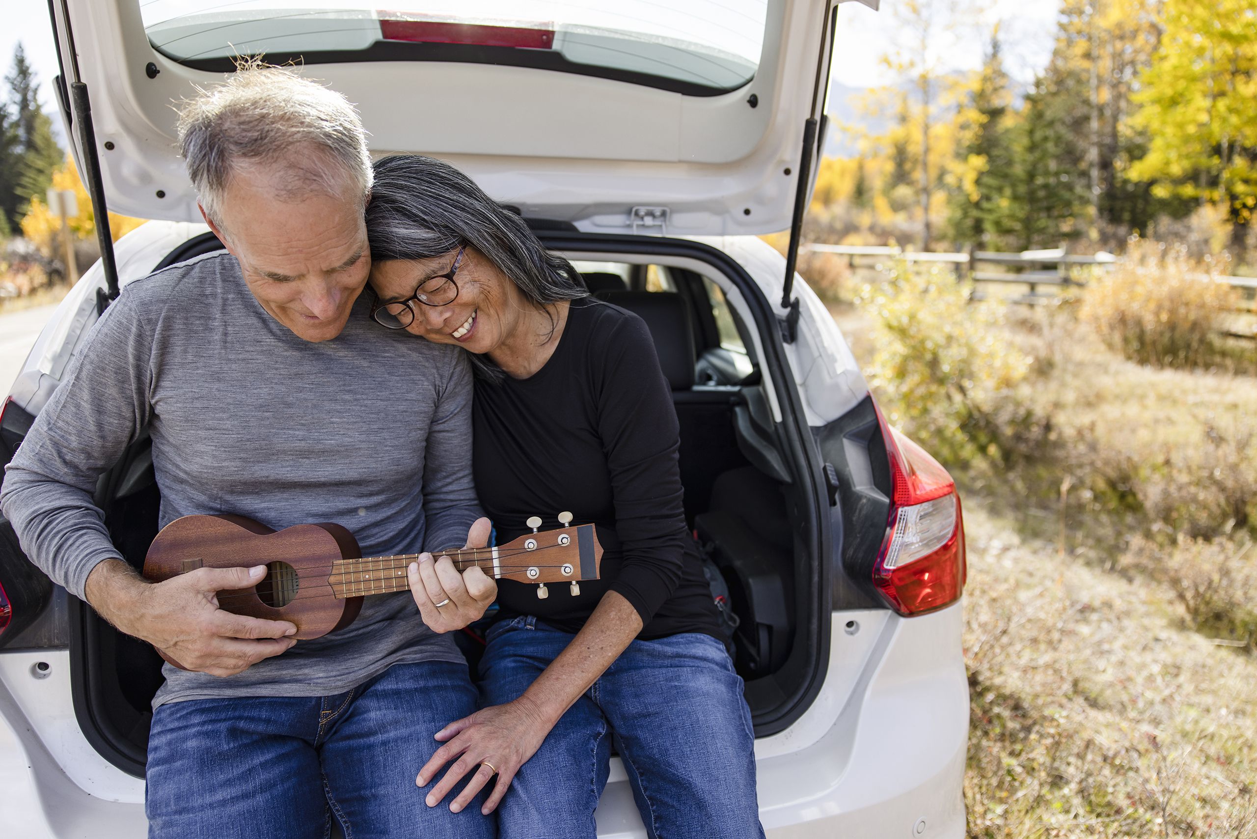 A happy couple outside playing the ukulele.