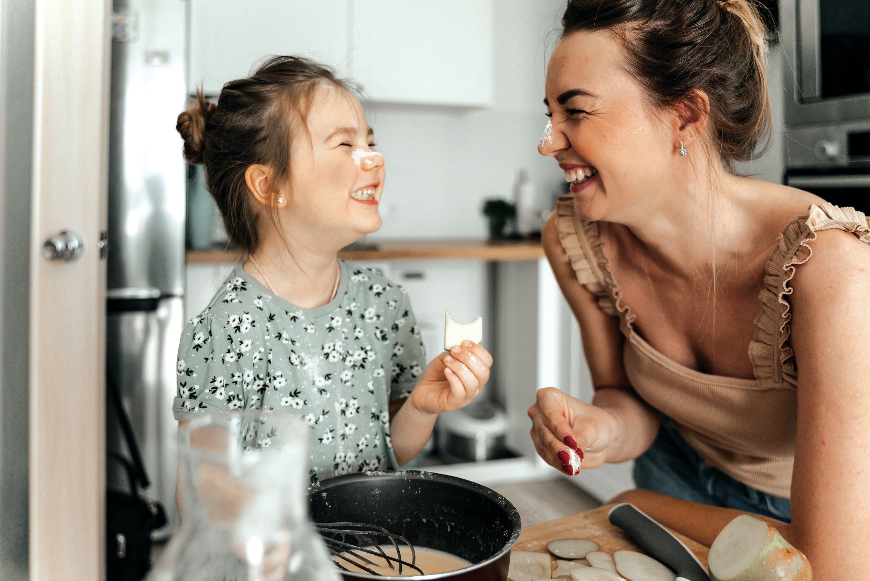 A mother and her child smiling and eating a cookie with flour on their nose.