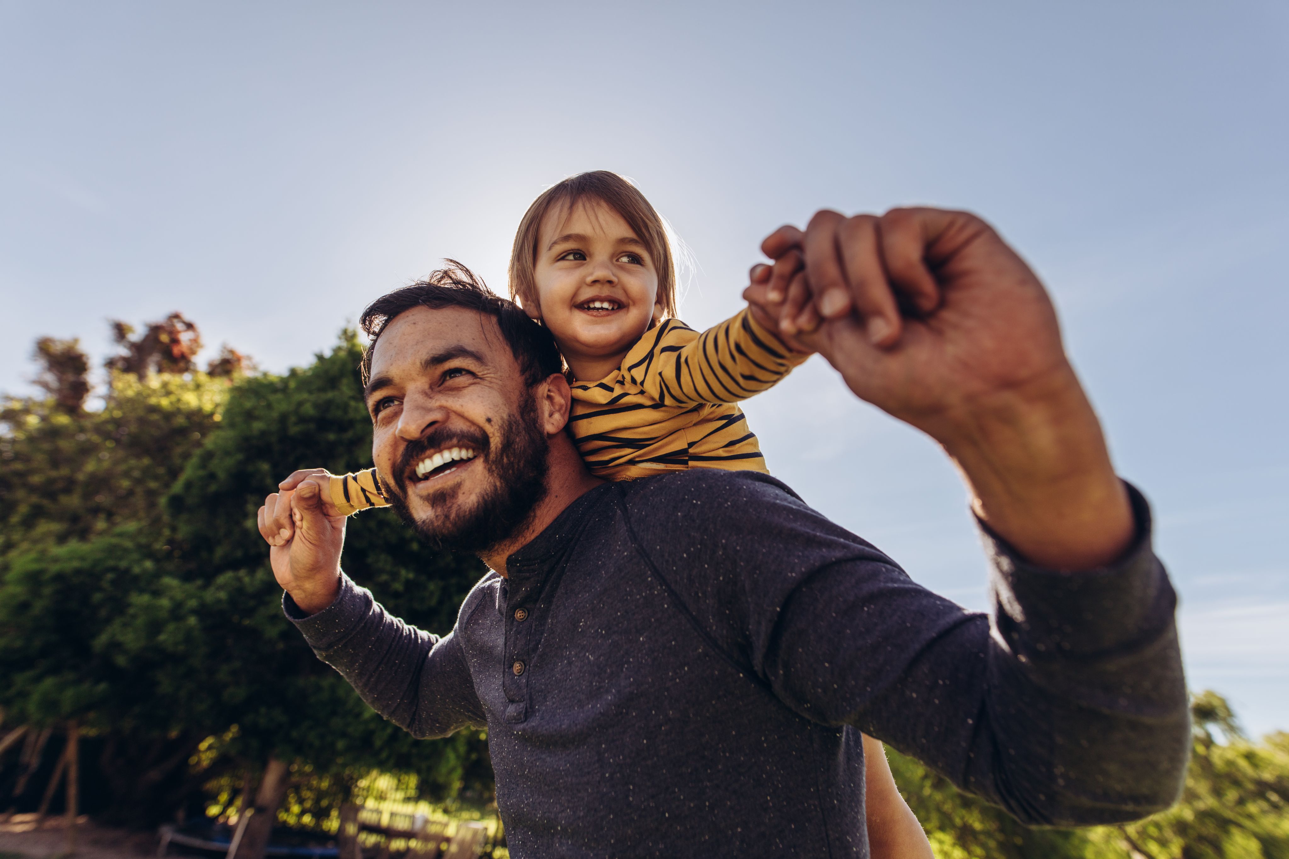 A man and small child laughing and holding hands in the sun. 