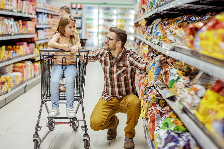 A man wearing glasses and his daughter in a grocery store snack section. 