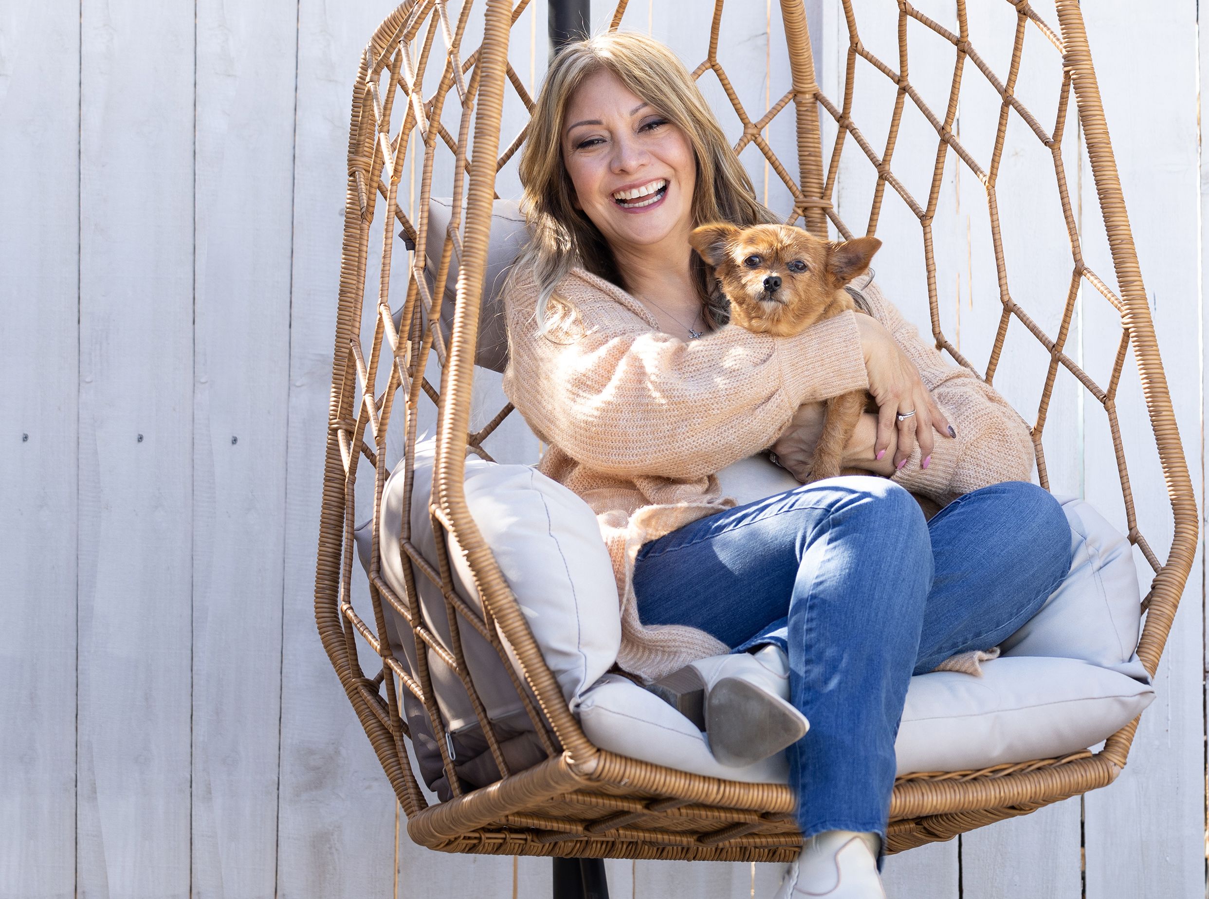 A woman with her dog smiling and sitting outside.