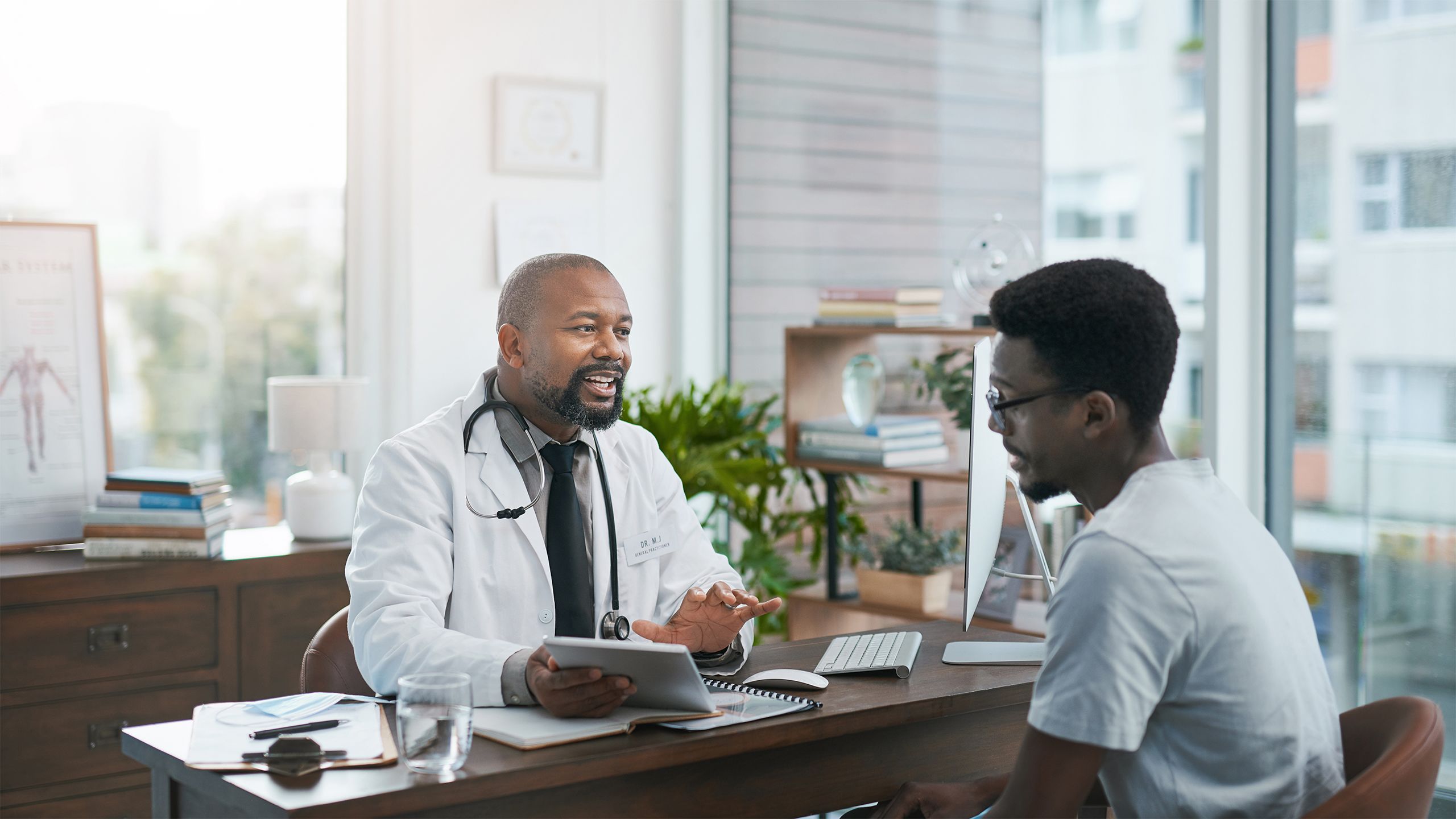 A Black doctor speaking with a young Black man at a desk