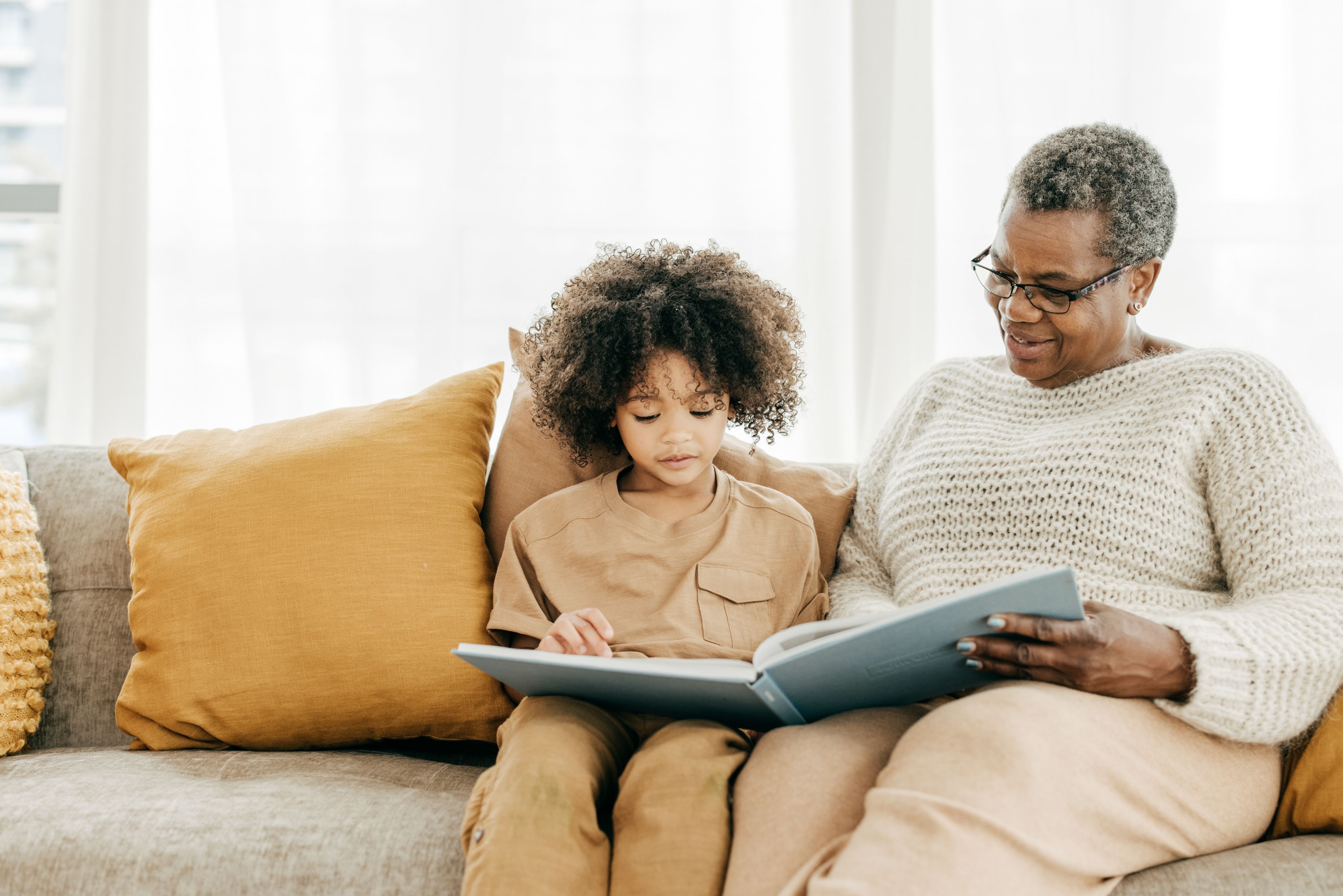 Older Black woman reading on couch with young child