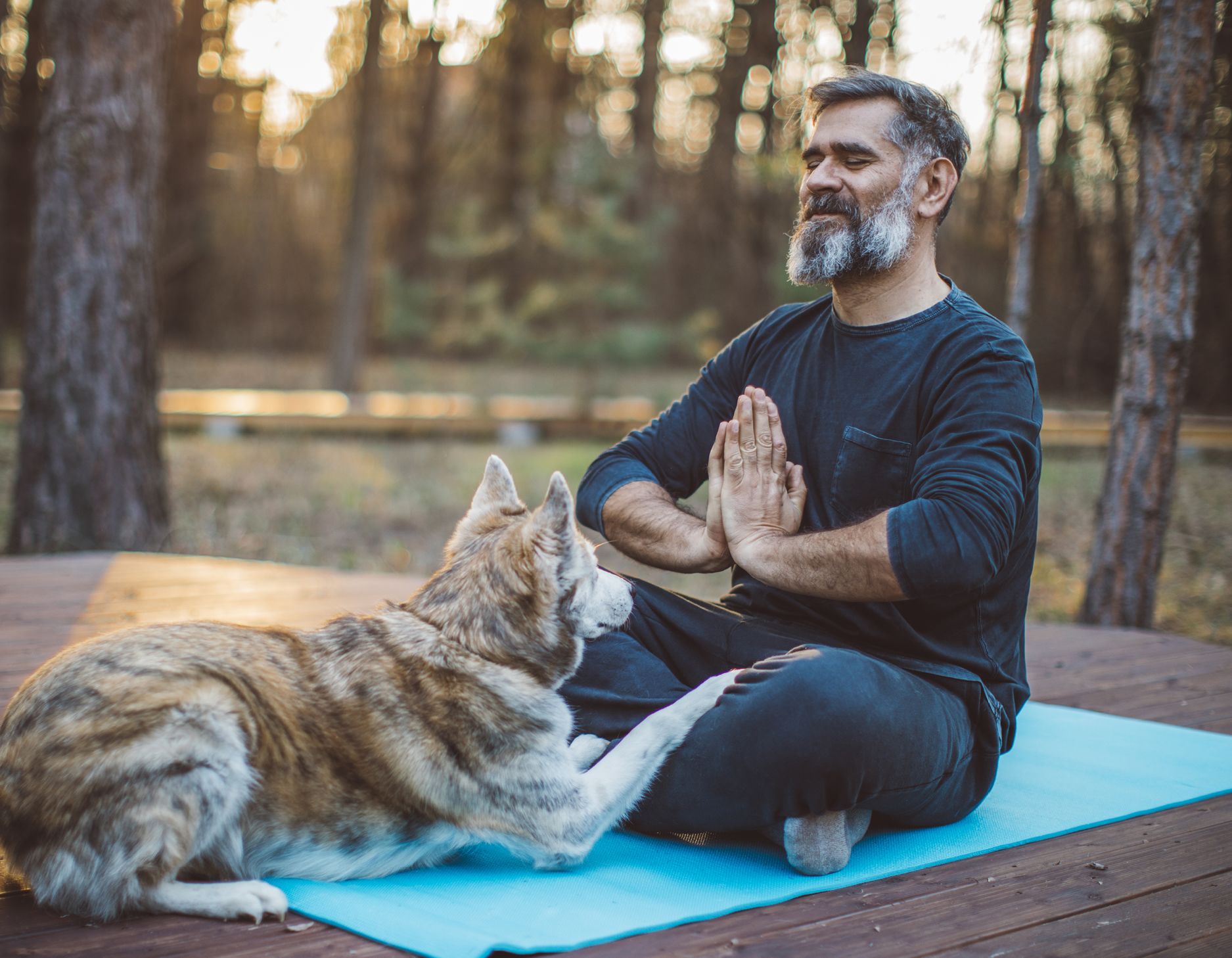 A man doing yoga outside with his dog.