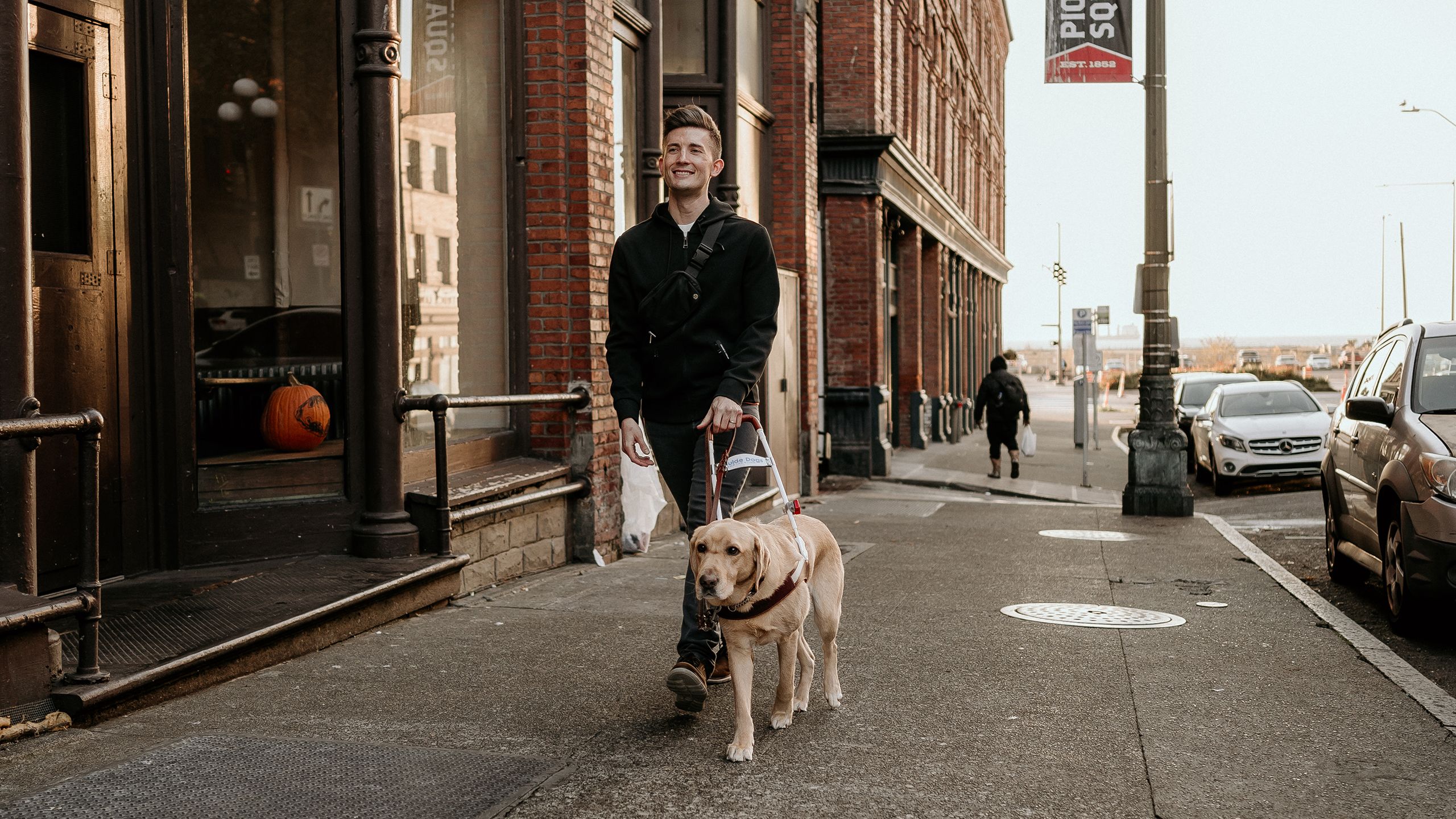 A man with IRD walking down the sidewalk with his seeing-eye dog.