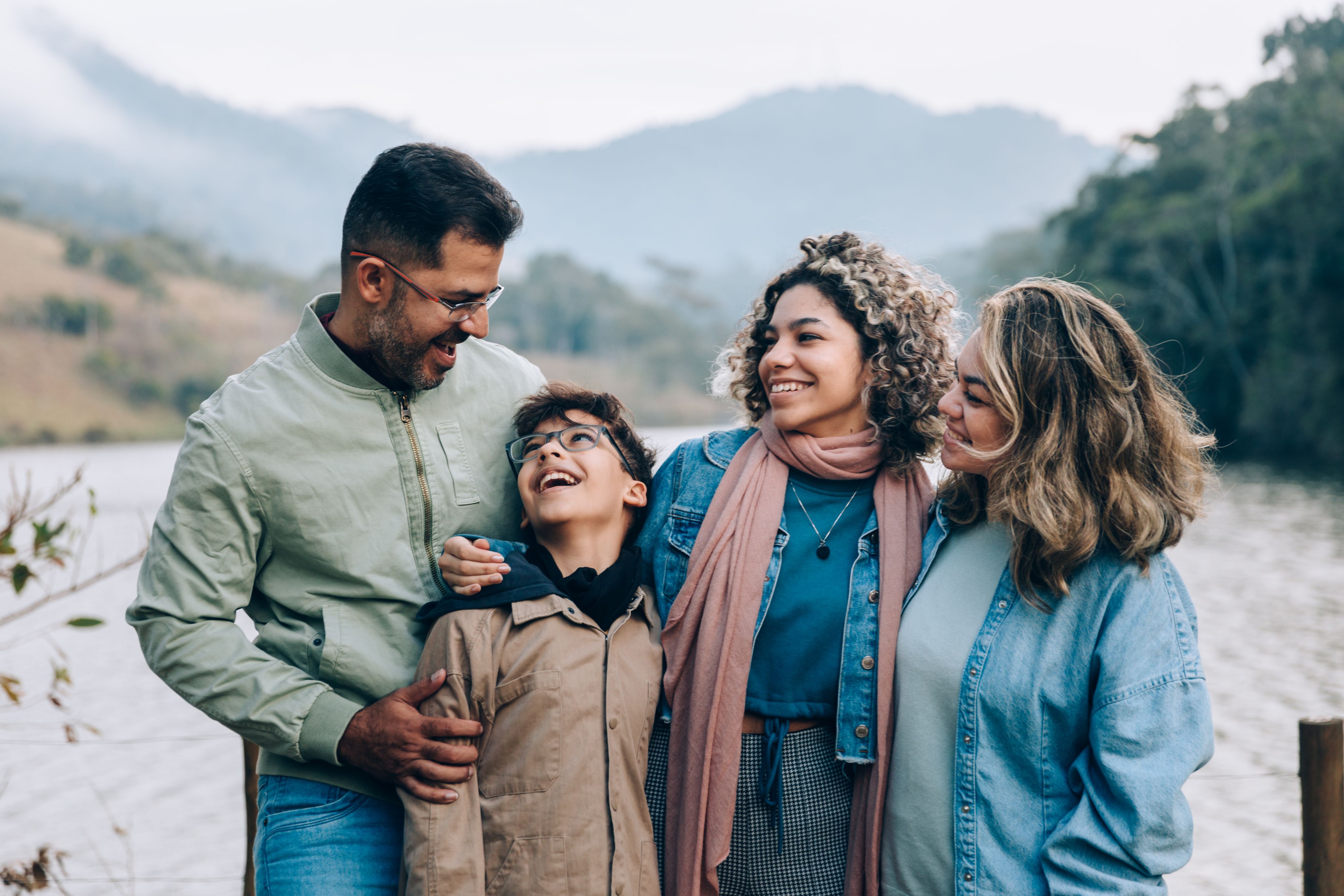 Family of 4 smiling at each other near a lake.
