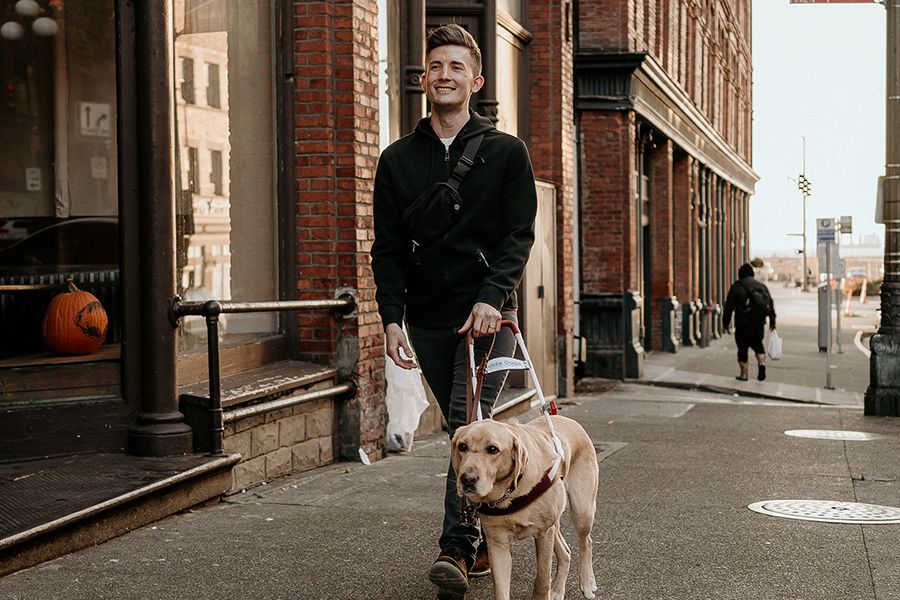 A man with IRD walking down the sidewalk with his seeing-eye dog. 