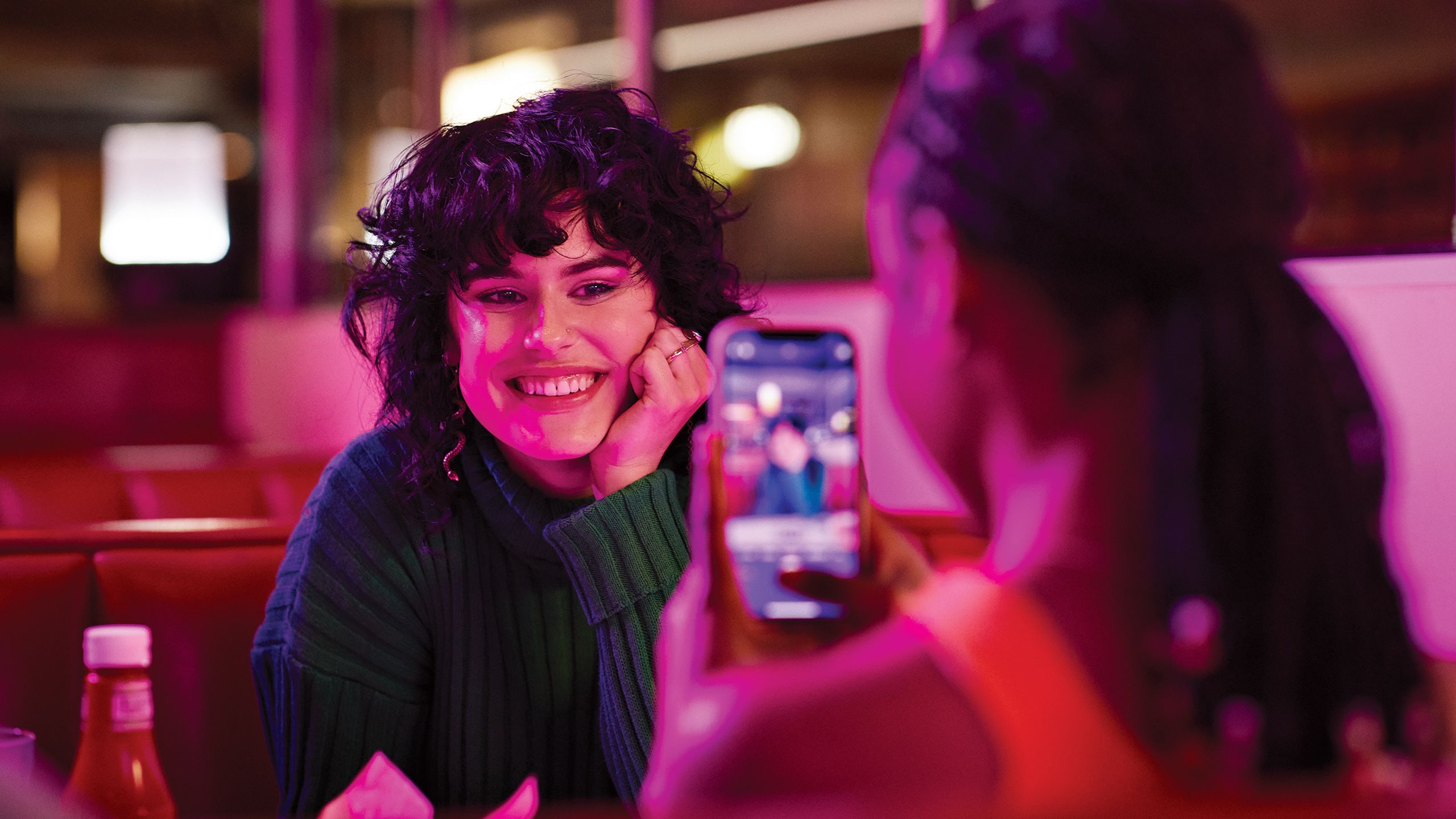 Woman taking a photo of another woman on her cellphone.