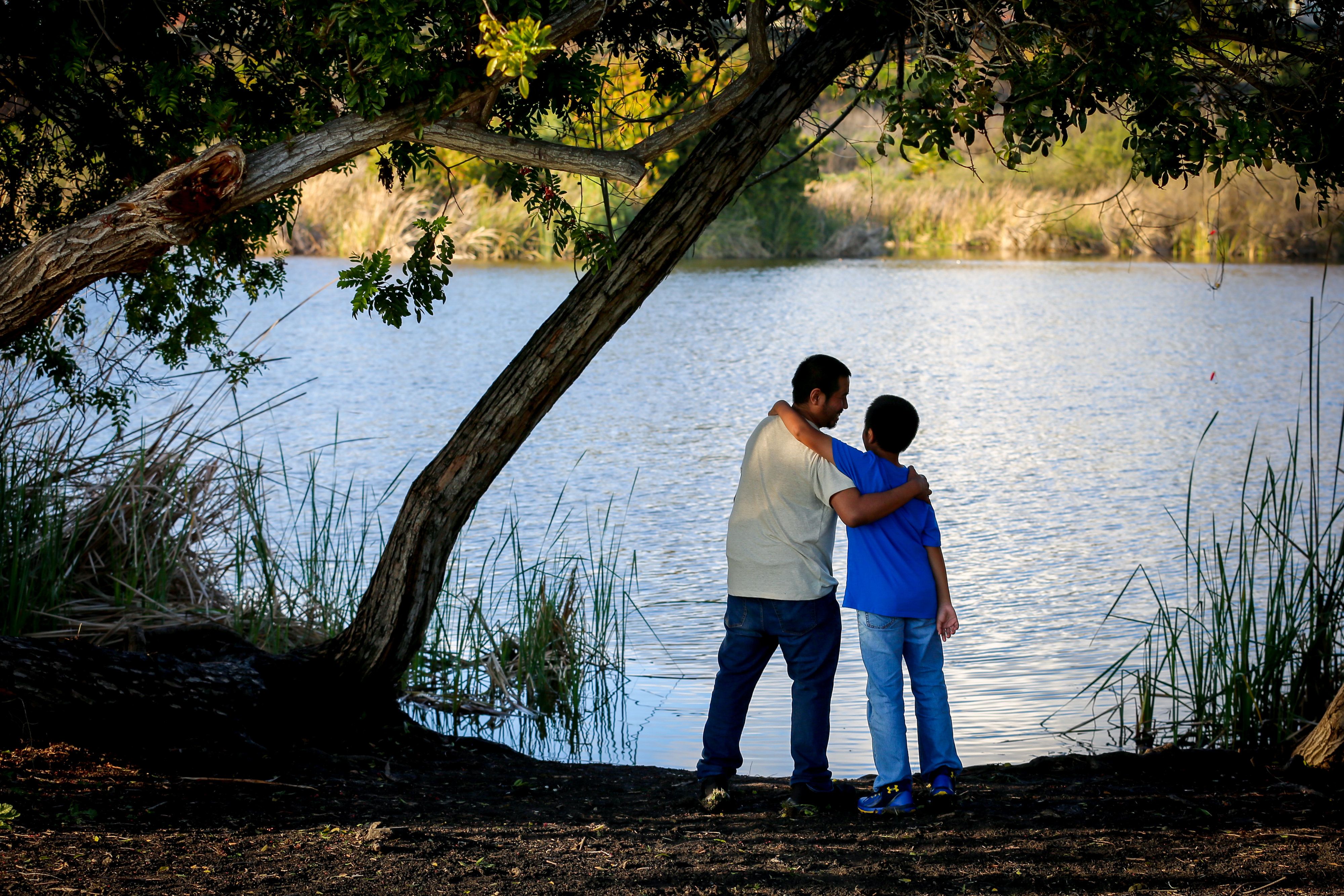 An image of father and son standing by a lake.